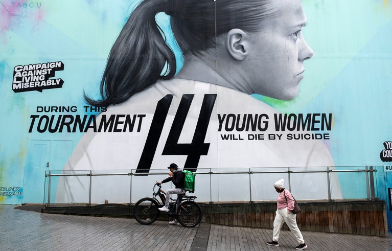 A pedestrian and cyclist go past a large poster of Fran Kirby promoting better mental health for women