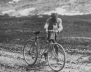 Photographie en noir et blanc d'un cycliste marchant à côté de sa bicyclette dans la montée d'un col.