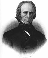 A man with thinning gray hair wearing a black jacket and time and white shirt