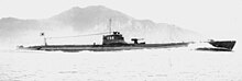 A World War II-era submarine in a body of water with a land mass in the background