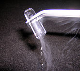 In a test tube held upside down by a set of pincers, there is what appears to be a plug of clear ice. A water-like liquid flows out of the bottom of the test tube, accompanied by some white vapour.