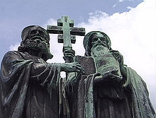 A photograph of statue, which depicts two bearded and hooded men, the one on the left is holding up a cross while the one on the right is holding up a book