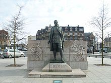 statue du roi en pied et en uniforme devant un mur de pierres sur lequel sont représentés le coq wallon et le lion flamand