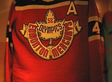 Un maillot rouge avec des bandes noires. Une feuille d'érable et les mots Edmonton Mercurys et 52 Olympics y figurent.