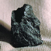 A small black rock with greenish overtones rests on a piece of fabric.