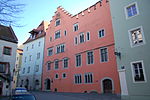 Several early modern or medieval townhouses. From right to left, a pale green house, a large red house filling most of the picture, and a white house.