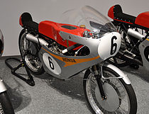 50cc-tweecilinder Honda RC 115 uit 1965. Het bijzondere aanzicht van het voorwiel wordt veroorzaakt door het gebruik van velgremmen.