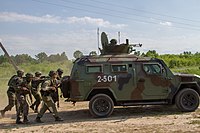 Soldados da Guarda Nacional em treinamento atrás de um veículo blindado KRAZ Cougar