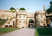 A paved road leading to a arched opening in a tall thick stone wall.