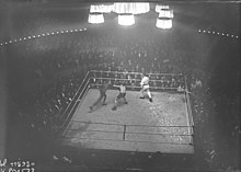 Photographie en noir et blanc prise de haut d'un combat de boxe.