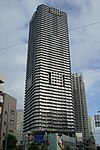 Ground-level view of a white, rectangular high-rise; the corners are cut and balconies form horizontal stripes up the height of the tower