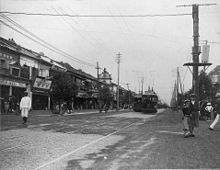 Photographie noir et blanc d'une rue de Tokyo en 1905. Au premier plan, une ligne de tramway à deux voies, un ciel nuageux en arrière-plan.