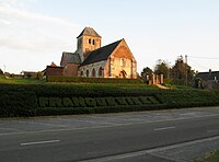 Léger surplomb de l'église. On remarque ses 2 niveaux successifs par rapport à la route. D'abord celui du cimetière, encore entouré de sa haie, auquel on accède par quelques marches.