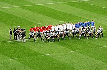 McCaw et les Néo-Zélandais en maillot gris interprètent le haka face aux joueurs français vêtus de bleu, blanc et rouge.