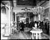 The interior of a home with several people gathered, but wearing winter coats. Ornate decorative features such as chandeliers and fancy rugs are visible