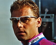 Photographie en gros plan d'un cycliste portant des lunettes et un maillot rose et bleu.