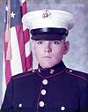 man in Marine uniform wearing cap, American flag in background