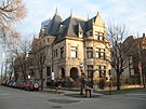 Three-story house on a street. Cars line the street and trees are barren in winter.