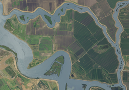 An aerial photograph of an island covered in farmland and surrounded by rivers. The island looks like a triceratops, facing left, being punched in the solar plexus from below.