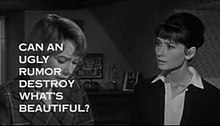 Still shot of a film trailer showing Shirley MacLaine looking down at the left and Audrey Hepburn to her right staring at her, in a bedroom. The words „Can an ugly rumor destroy what's beautiful?“ obscure much of MacLaine's face