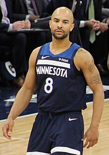 Thirty-year-old man with shaved head, moustache and goatee wearing navy blue Timberwolves uniform, appears to be backing up