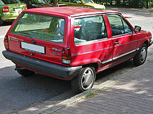 Rear-three-quarter view of a small three-door car with a flat roof, black-plastic bumpers, door mirrors, a sunroof, and hubcaps.