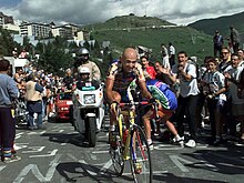 Photographie d'un cycliste suivi d'une moto et entouré par la foule dans une ascension.