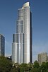 tall silver skyscraper with blue sky background beyond tall trees