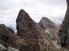 Rugged mountain scenery. Several sharp prominences of bare grey rock stand out on a long ridge leading to more hills beyond.