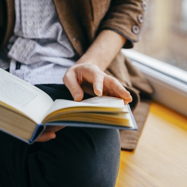 A person sits on a window ledge, while reading a book