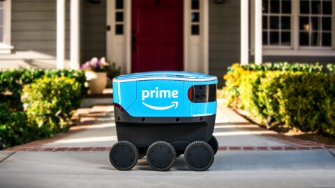 A small blue delivery bot with Amazon Prime branding sits on a walkway that leads to a house. 