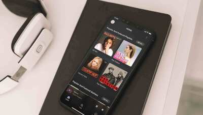 Amazon Music app on an iPhone X displayed on a notebook next to a pair of headphones.