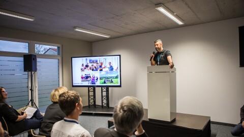 Beim Open House in Tübingen wurden verschiede Vorträge gehalten. Die Gäste sitzen auf Stühlen und schauen sich die Präsentationen auf einem Bildschirm ein.