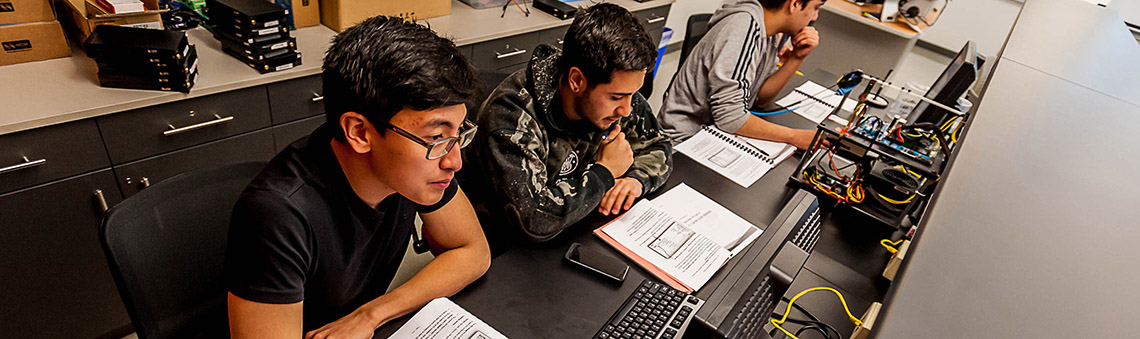 three male students in front of computers