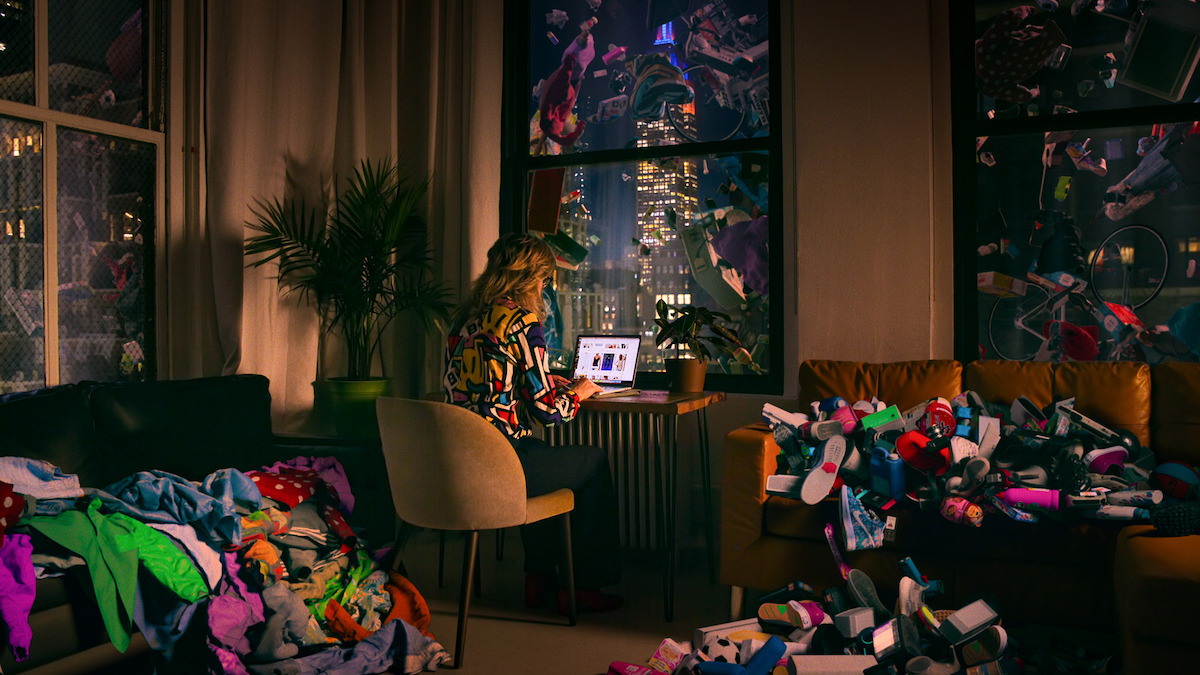 A woman is at her computer shopping while products are strewn across her room.