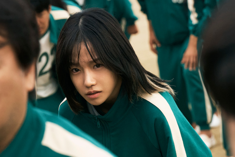 A woman stands in a crowd wearing a green track suit in 'Squid Game' Season 2 