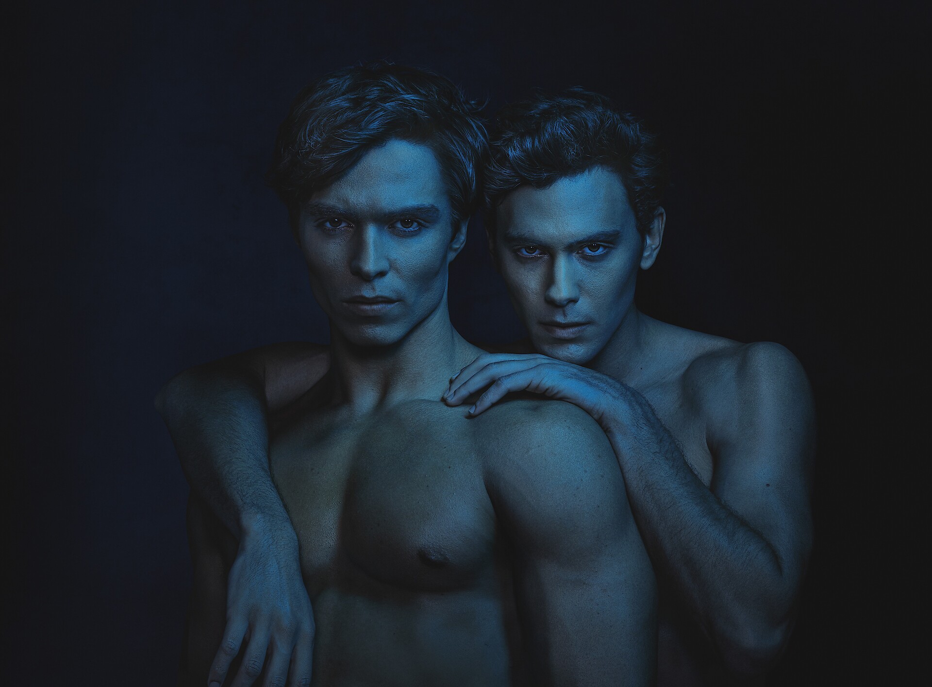 The characters of Erik and Lyle Menendez posing shirtless against a dark blue and black background