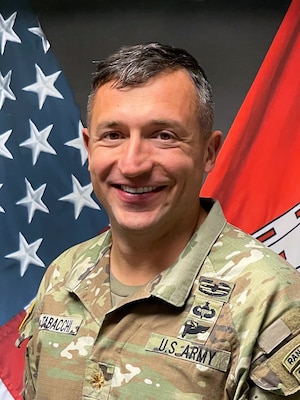 An army officer standing in front of a U.S. flag.