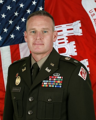 Head and shoulders portrait photo with American and U.S. Army Corps of Engineers flag in the background.