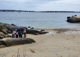 A group of student trainees stand in a group along a Massachusetts shoreline.