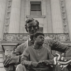 A boy sitting on the lap of a statue of Abraham Lincoln