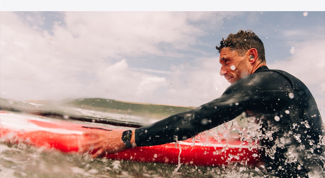 A man in a wetsuit wearing an Apple Watch Series 10 preparing to paddle out in the surf.