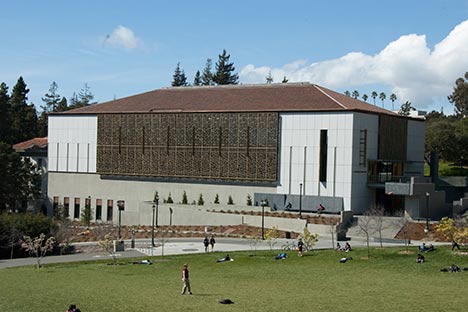 Large building with decorative metal window screen. Large grassy area with people.