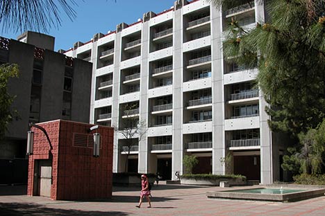 Large building with small reddish building, reflection pool, and person walking in front