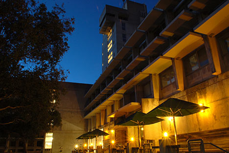 Illuminated tables with umbrellas in front of large building with night sky