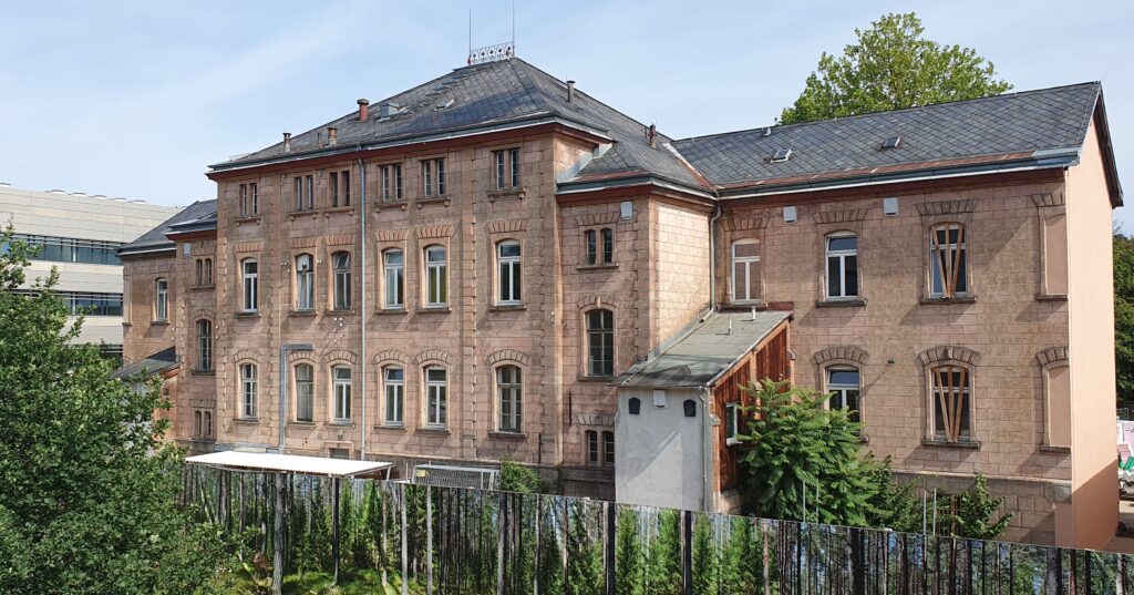 Ein gebäude aus rotem Sandstein hinter eienm Zaun. Heil- und Pflegeanstalt Erlangen Hupfla