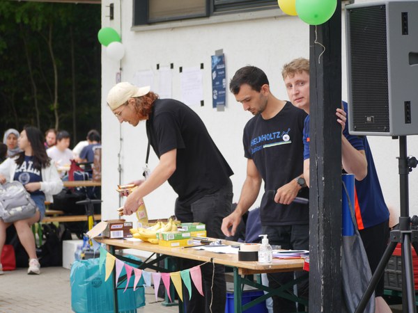 Julian, Johannes and Markus are standing at a stand with snacks. They are  at the DocTeam summer party. 