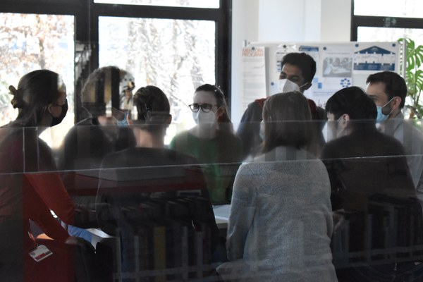 Eight peüple with masks are at a DocTeam Meeting. They are standing around a table.