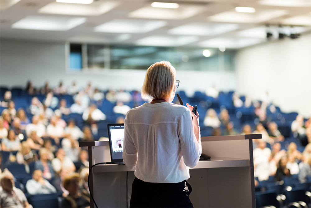 Eine Professorin hält einen Vortrag vor einem vollen Hörsaal.