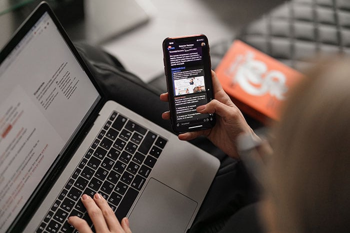 Person using a mobile with a Twitter feed, and a laptop